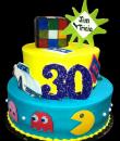 Totally 80's Birthday cake,  Blue and yellow buttercream iced, 2 round tiers with 80's memorable. Decorated with the fun Rubik's cube, the original pacman, cassette tapes, and of course, a corvette.  Everything on this cake is EDIBLE. (Serves 28-55 party slices)